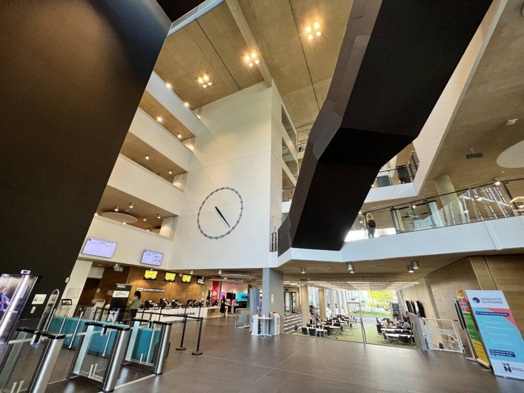 A giant clocks sits in the central void of the learning hub. A staircase cuts across it at level 1 through to 2.